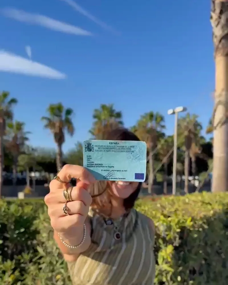 Een klant laat haar groene residencia-certificaat zien, onder de palmen van Valencia
